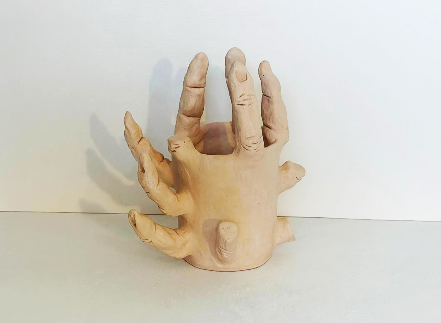 Severed fingers, the same ceramic hand vessel seen from a second angle, fingers splayed outward