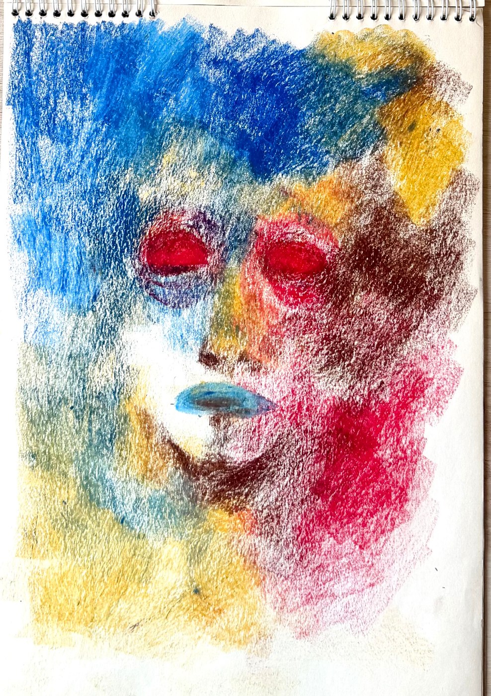 Self-portrait study in oil pastel, a face dissolving into blue, red and yellow